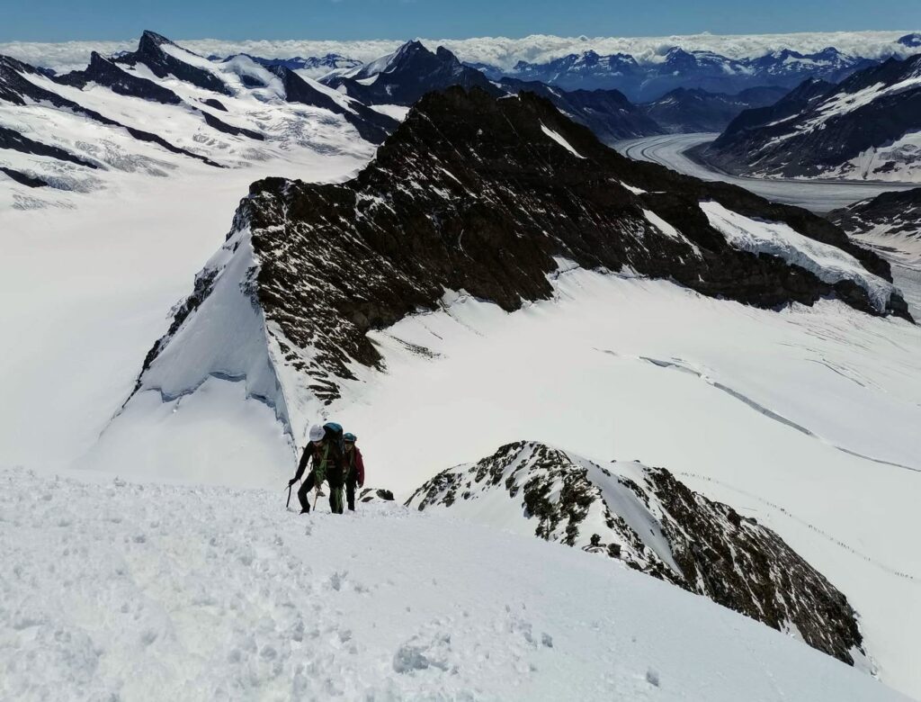 Melanie Shudofsky (Leadership Development Coach) leading another mountaineer on a steep snowy mountain face against the backdrop of a glacier.